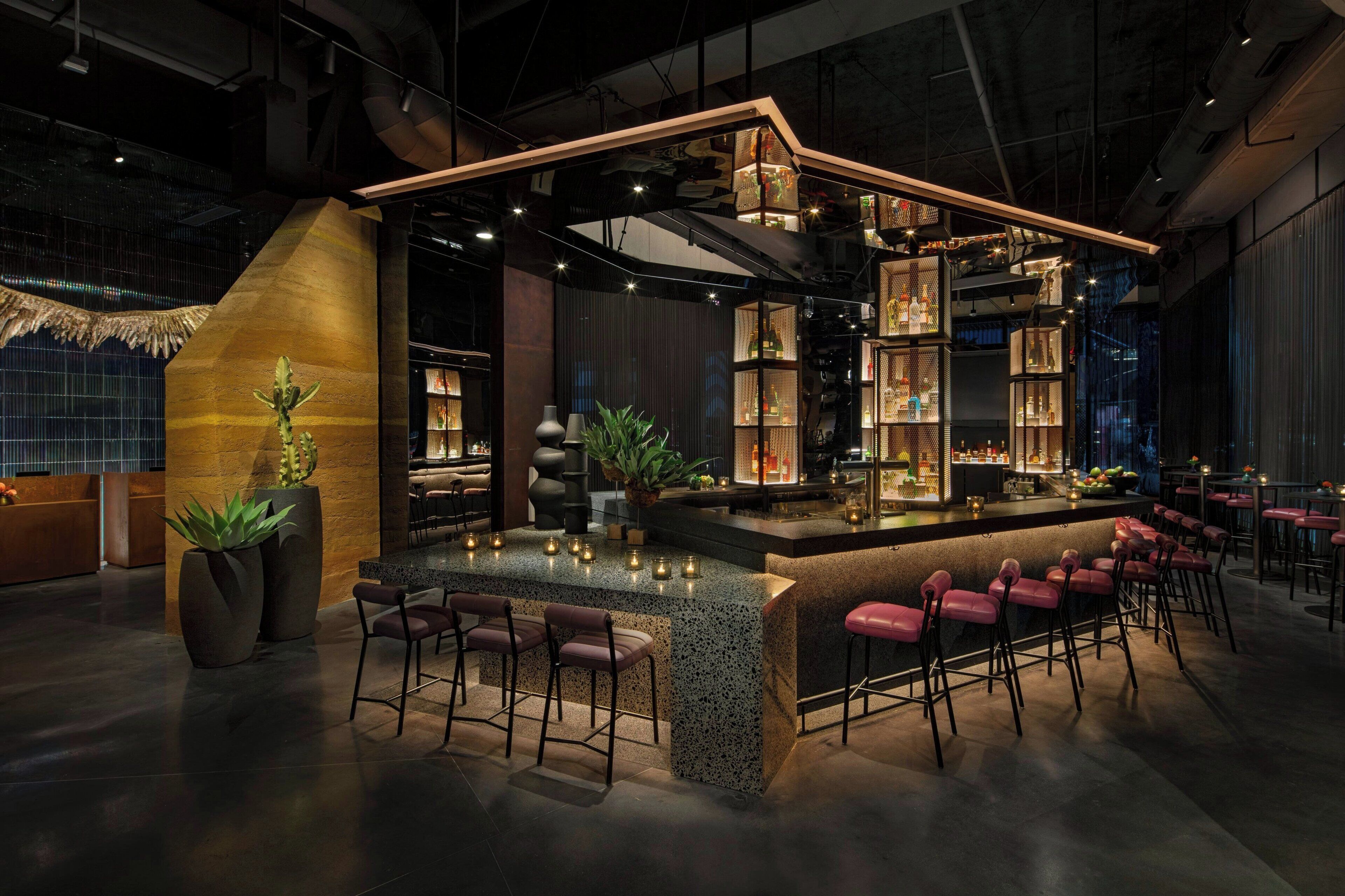 A modern bar area with a central island, bar stools, and shelves stocked with bottles.