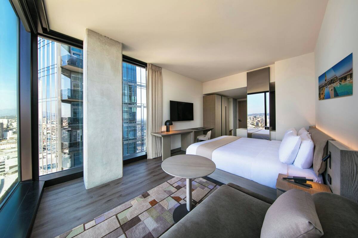 A modern hotel room with a large bed, a desk, a small round table, and a TV.