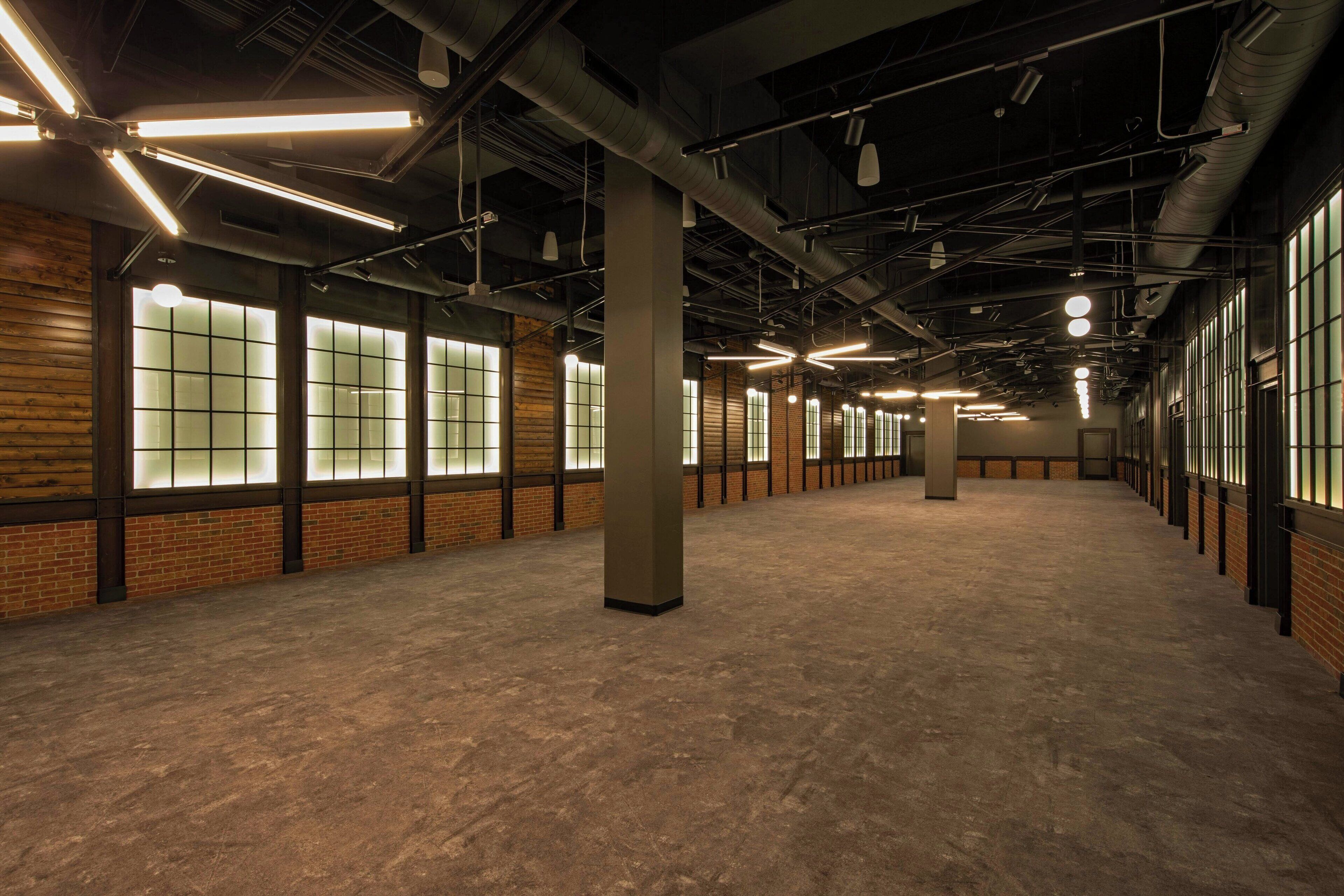 Un intérieur spacieux de style industriel, avec des murs en briques apparentes, de grandes fenêtres et un sol en béton.