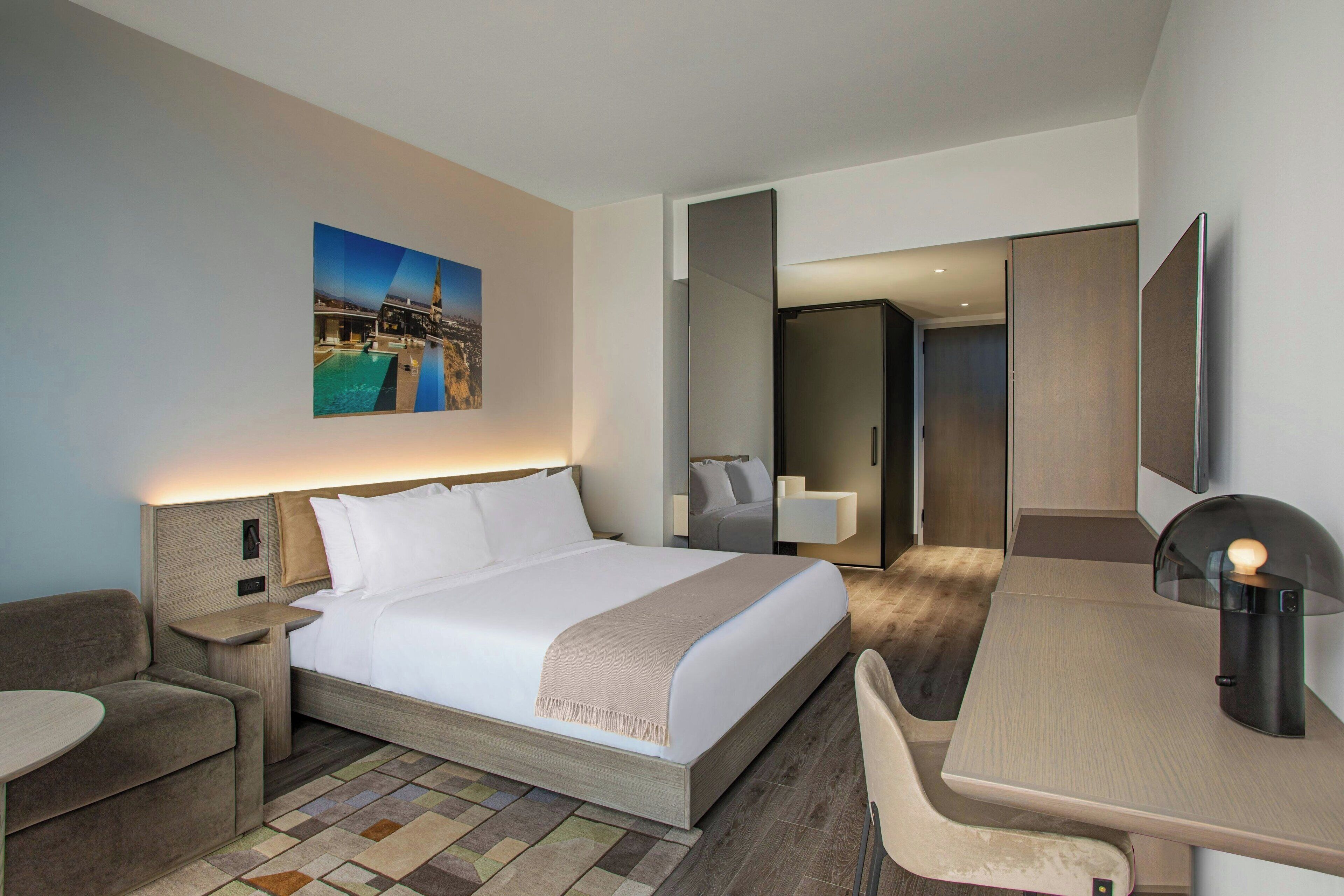 Une chambre d’hôtel moderne, dotée d’un grand lit, d’un bureau, d’une chaise, d’une petite table et d’un tableau au mur.