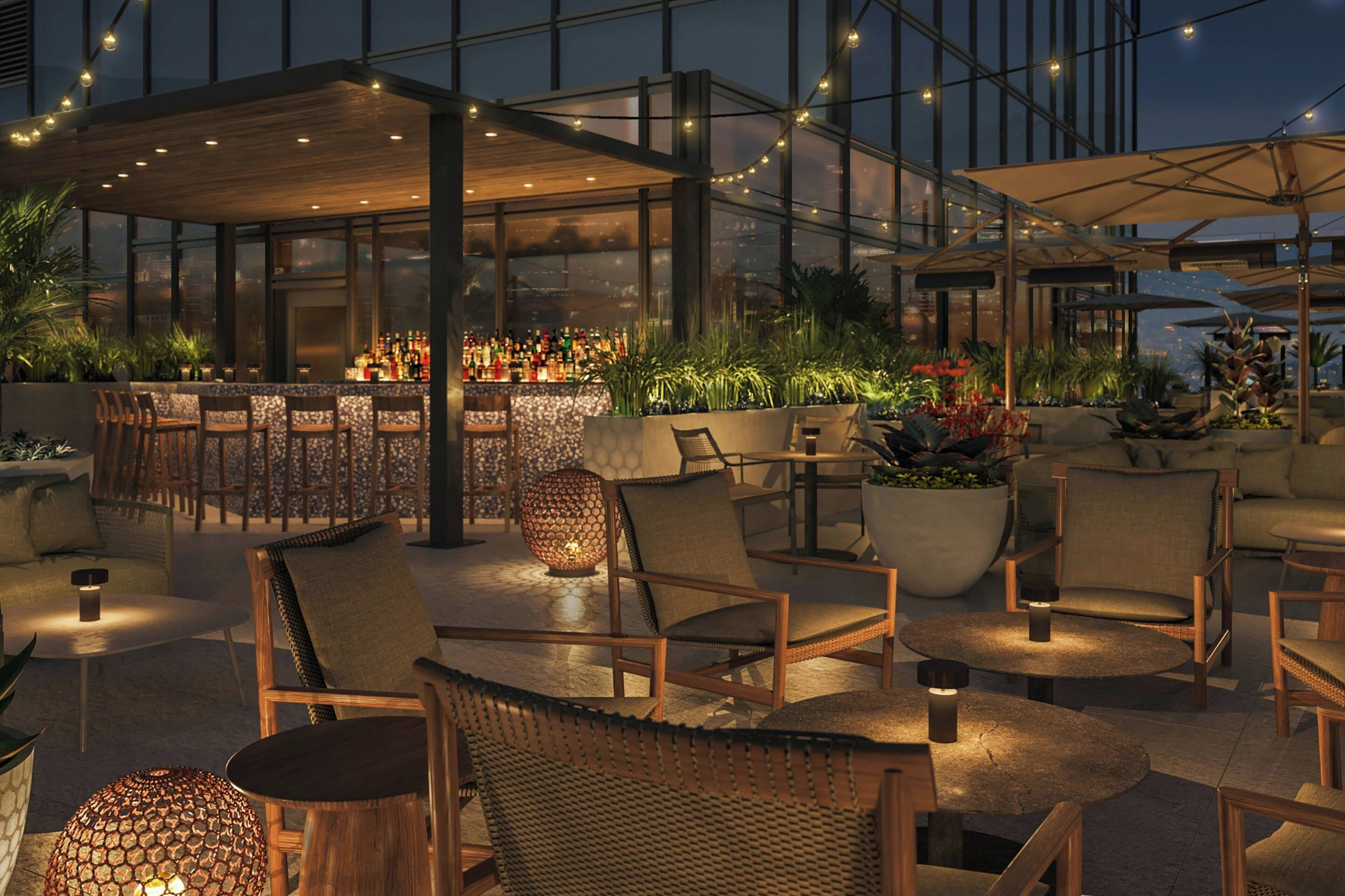 An outdoor seating area with wooden chairs and tables, a bar with bottles, and potted plants.