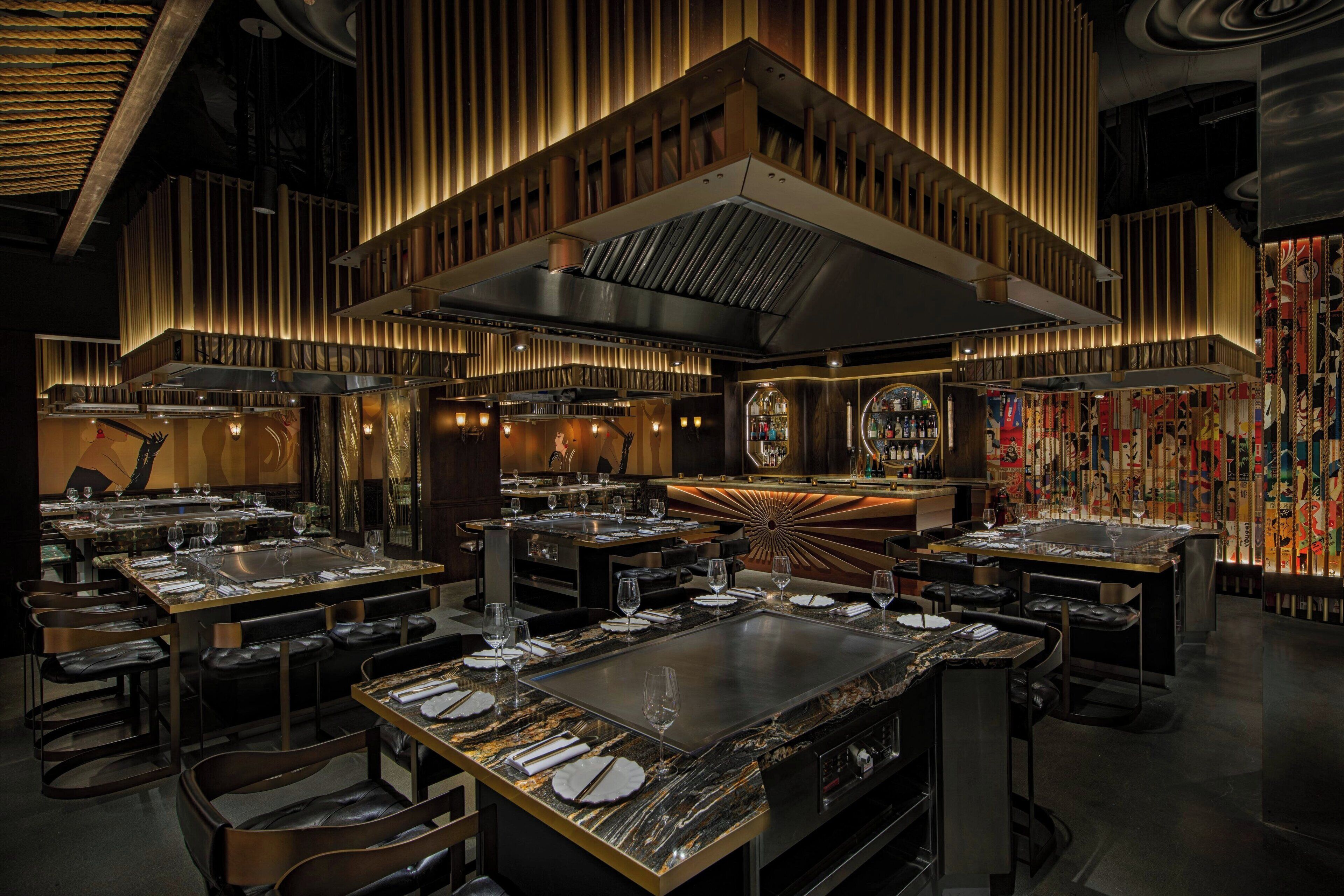 A modern restaurant with multiple dining tables, a central bar area, and a decorative ceiling.