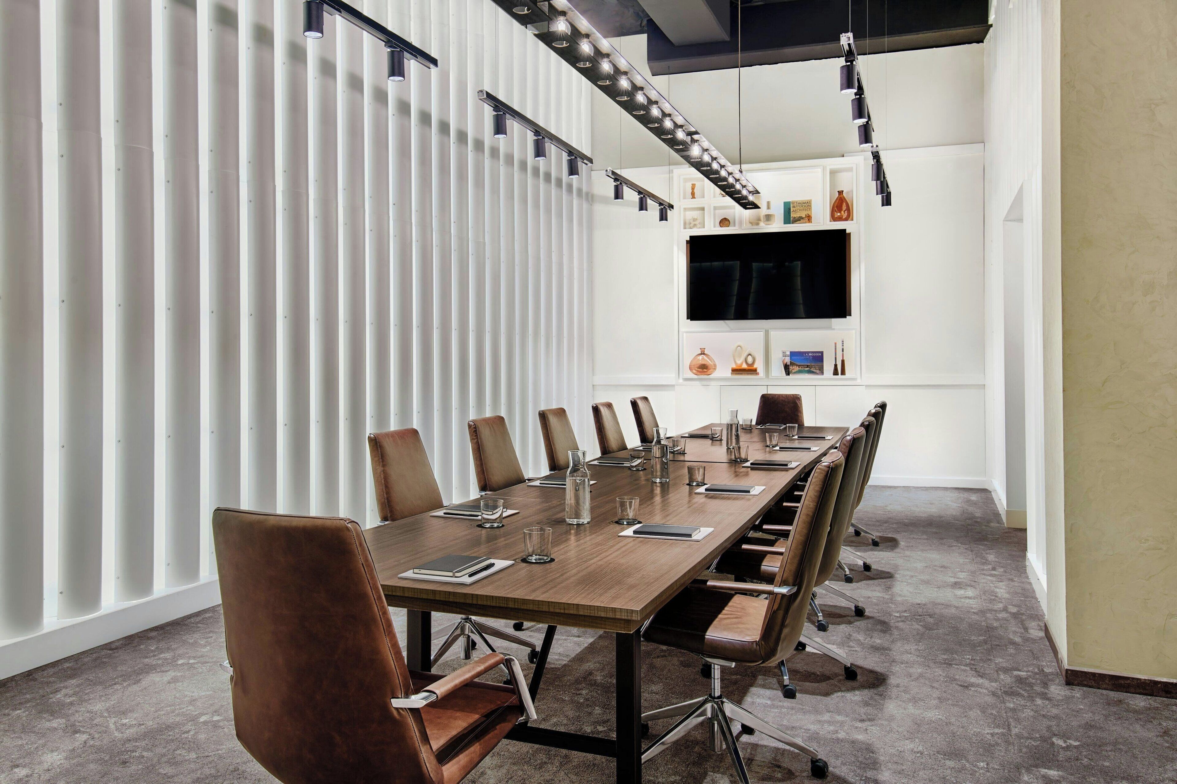 A conference room with a long table, chairs, a TV, and a whiteboard.