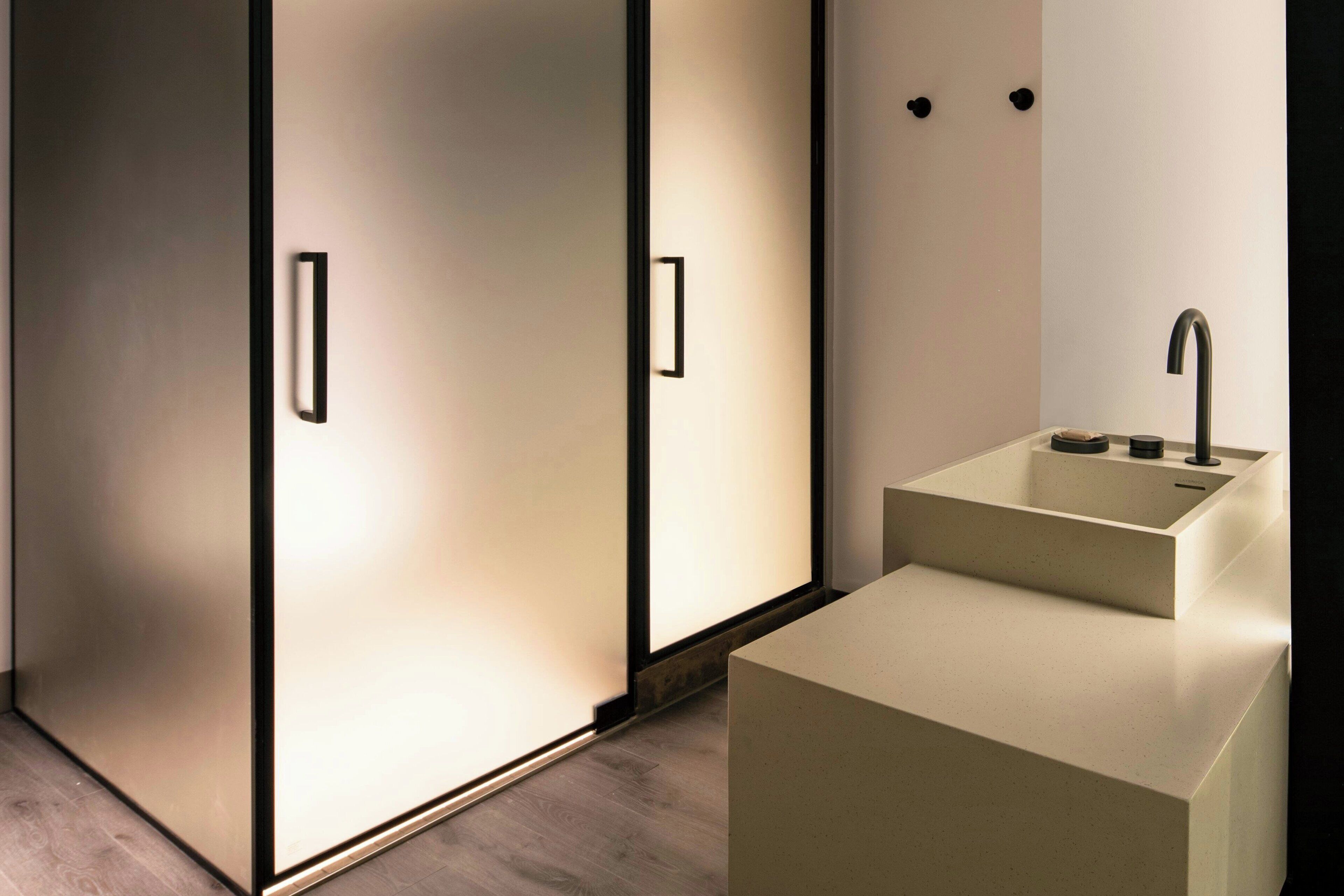 A modern bathroom with a minimalist design, featuring a large mirror, a pedestal sink, and a walk-in shower.