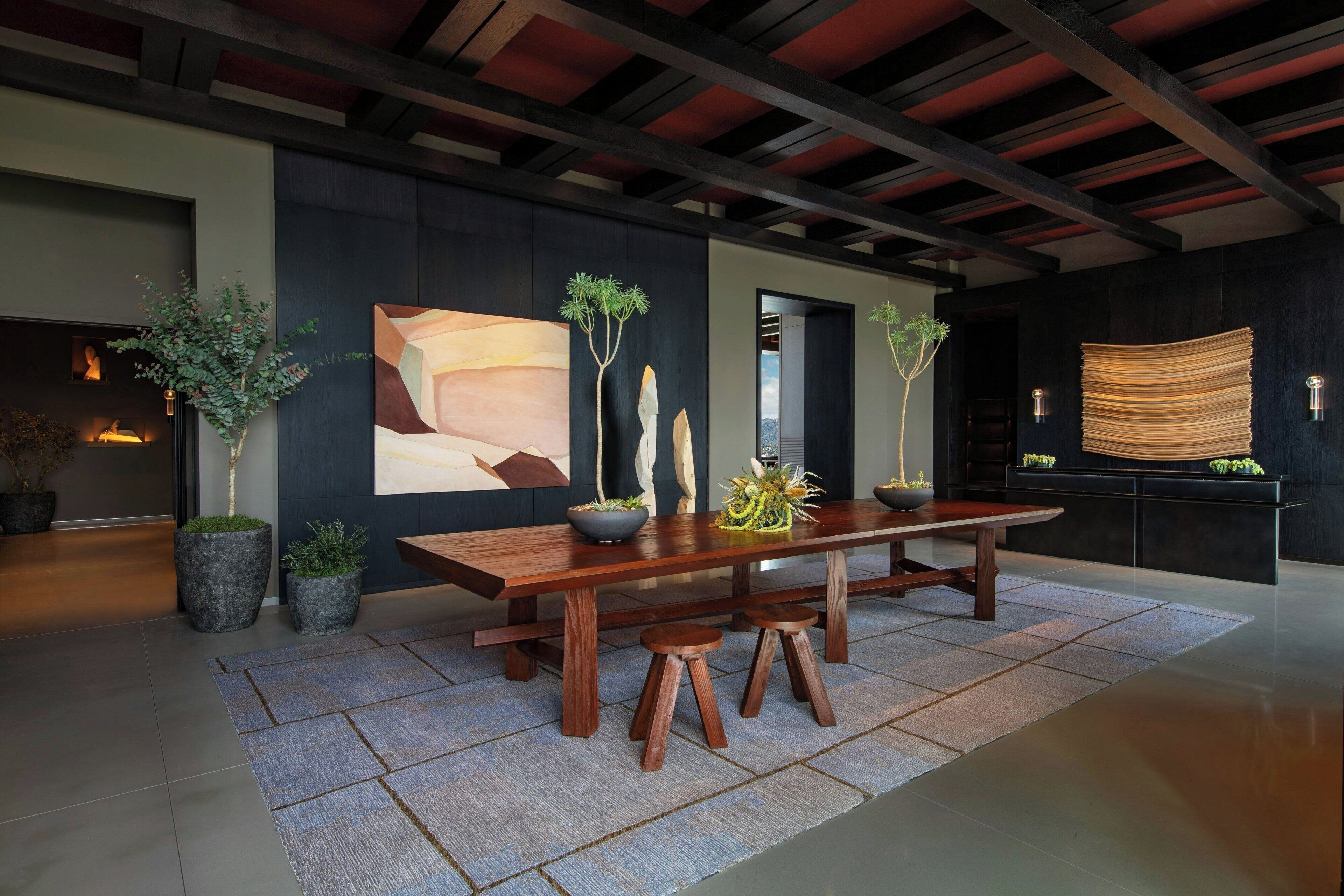 A modern dining area with a wooden table, stools, and potted plants.