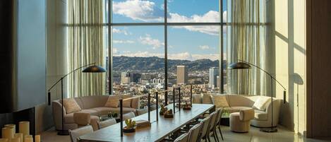 A spacious living room with a large window offering a city view, a long dining table, and modern furniture.