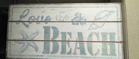 A rustic wooden sign with the text "Love the Beach" and decorative elements like a starfish and seashells.