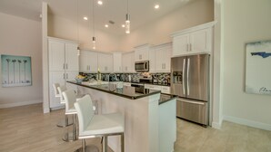 Una cocina moderna con armarios blancos, electrodomésticos de acero inoxidable y una isla central con taburetes de bar.