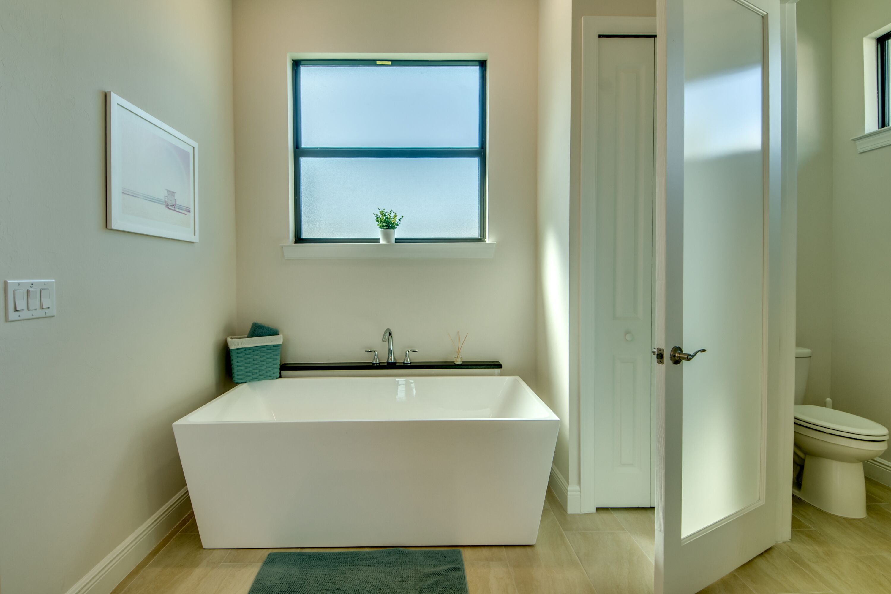 A modern bathroom with a freestanding bathtub, a window with a view, and a toilet.