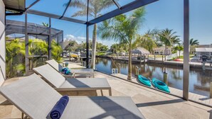 Un espacio exterior techado con sillones, una mesa y vistas a un canal con barcos.