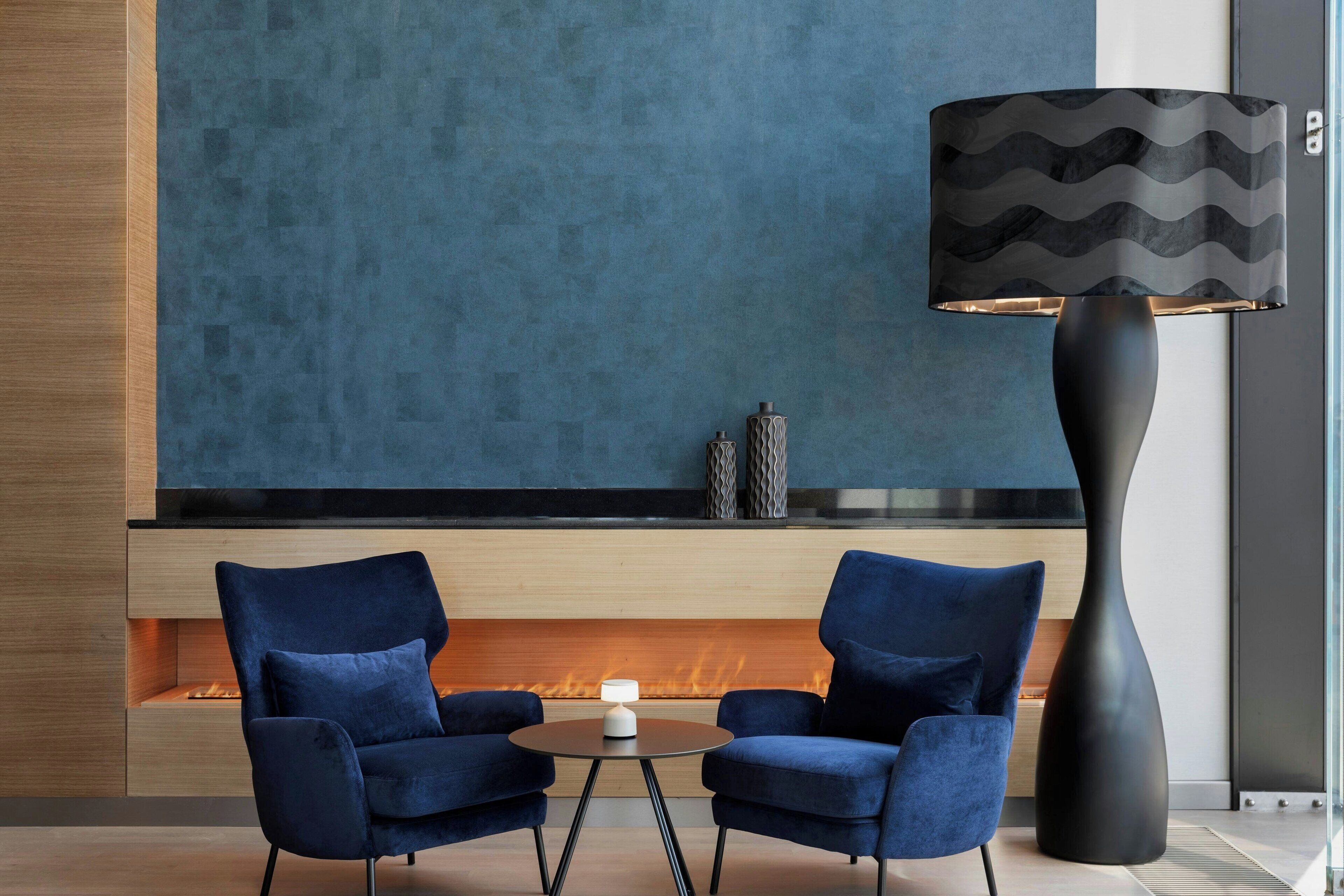 Un área de estar moderna con dos sillones azules, una mesa redonda, una lámpara de pie negra y una chimenea.