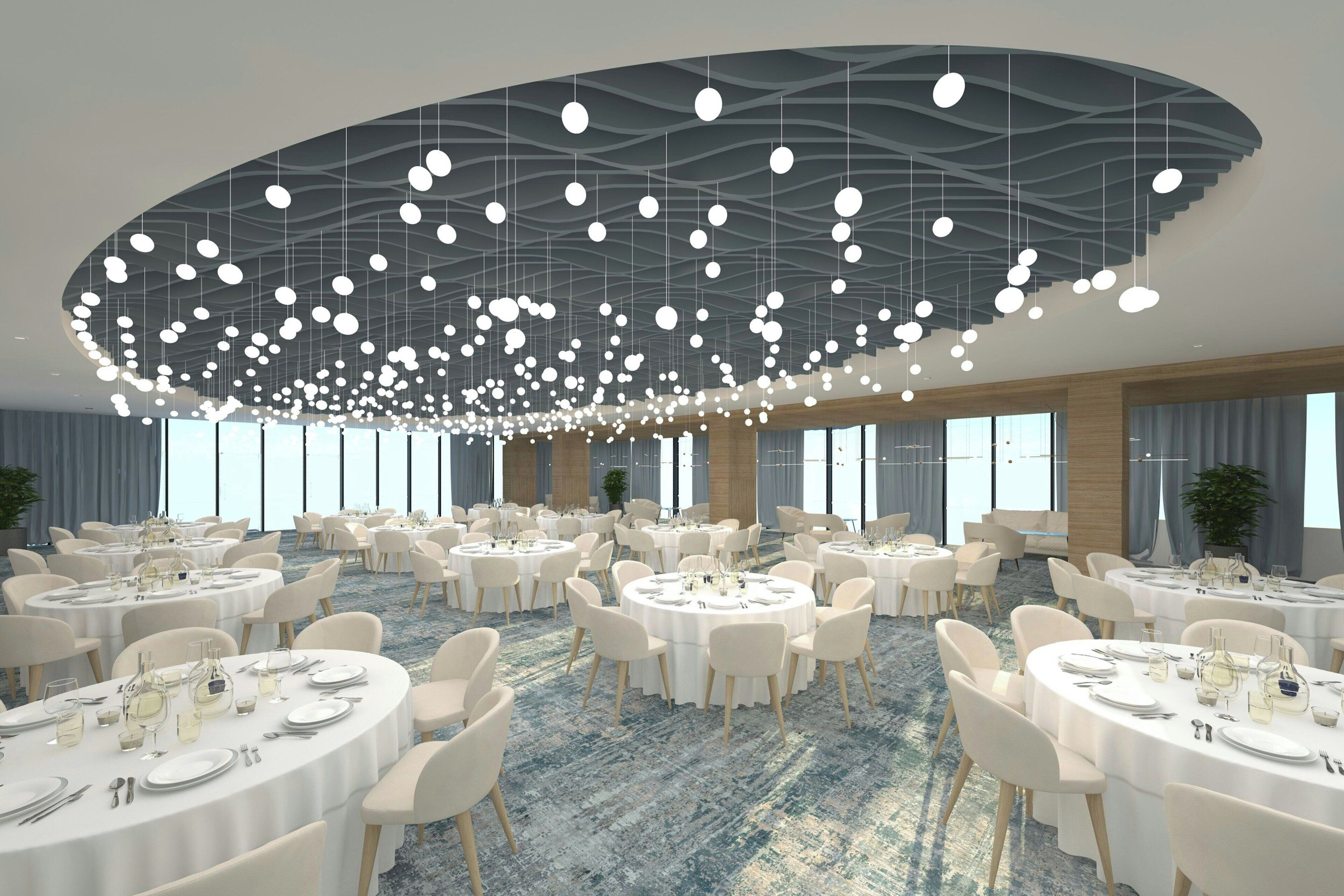 A spacious conference room with round tables, white chairs, and a modern ceiling design with hanging lights.