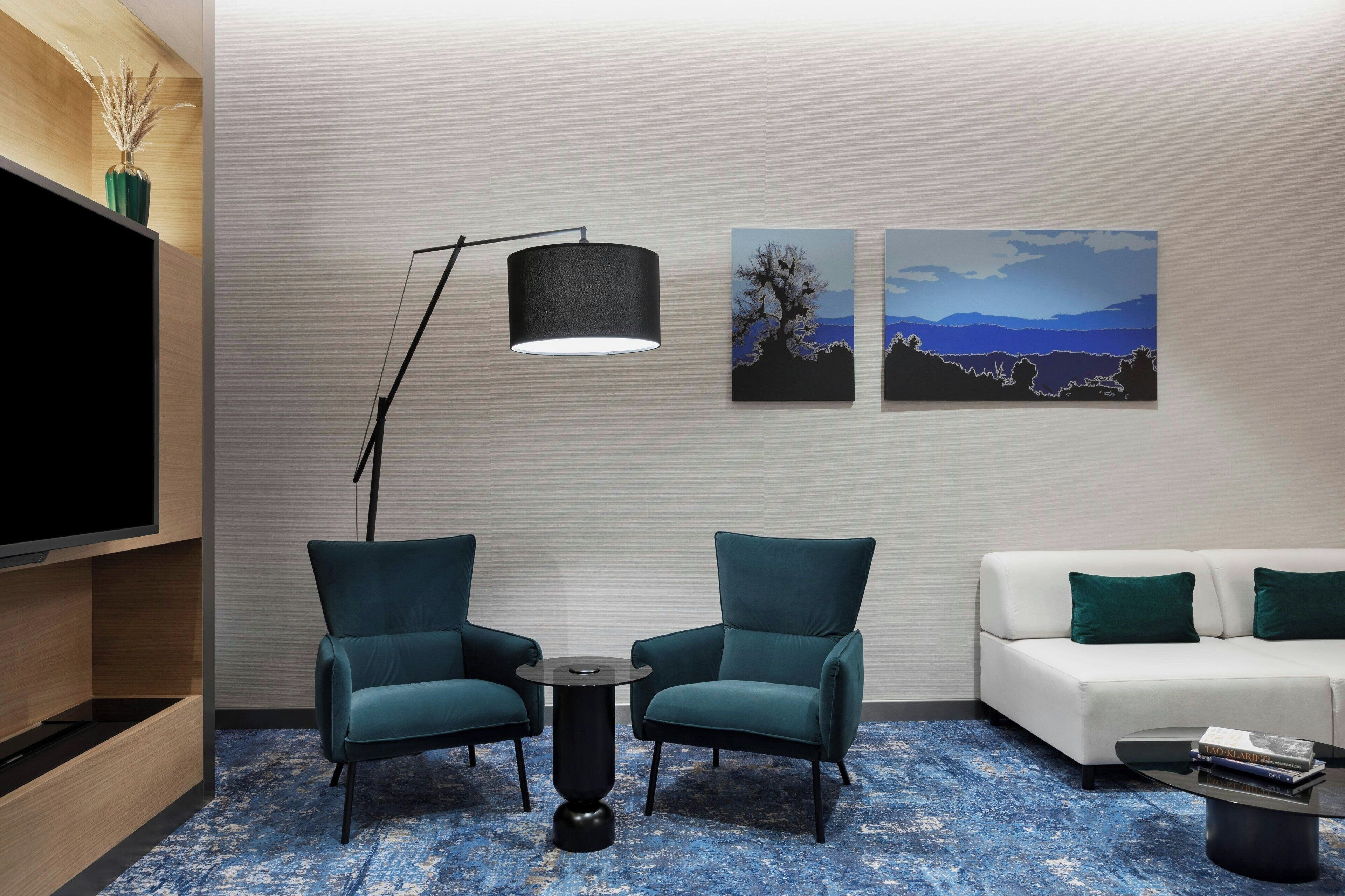 Una sala de estar moderna con dos sillones color turquesa, un sofá blanco, una lámpara de pie negra y un televisor de pantalla plana.