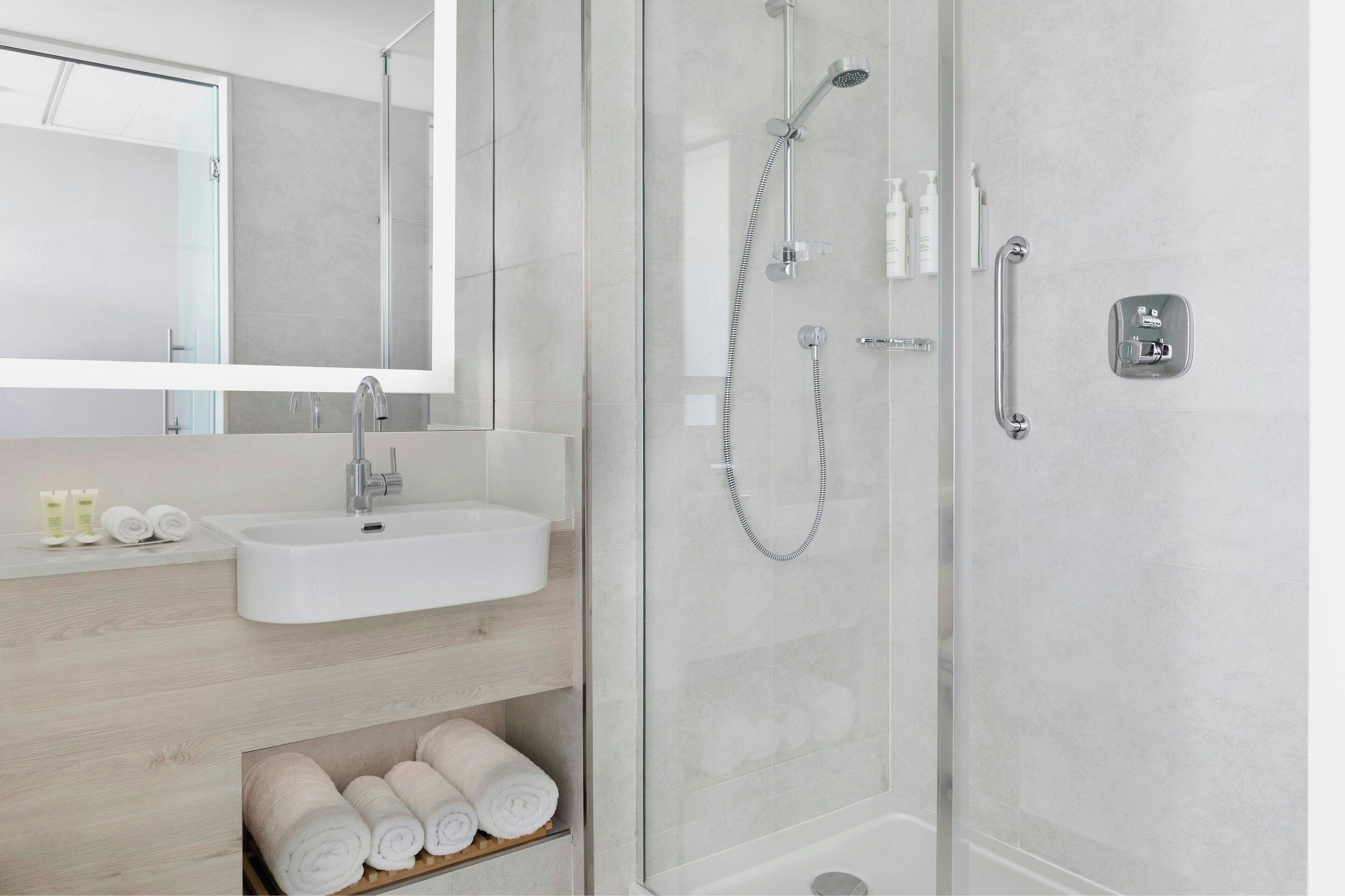 A modern bathroom with a glass-enclosed shower, a white sink, and a mirror above it.