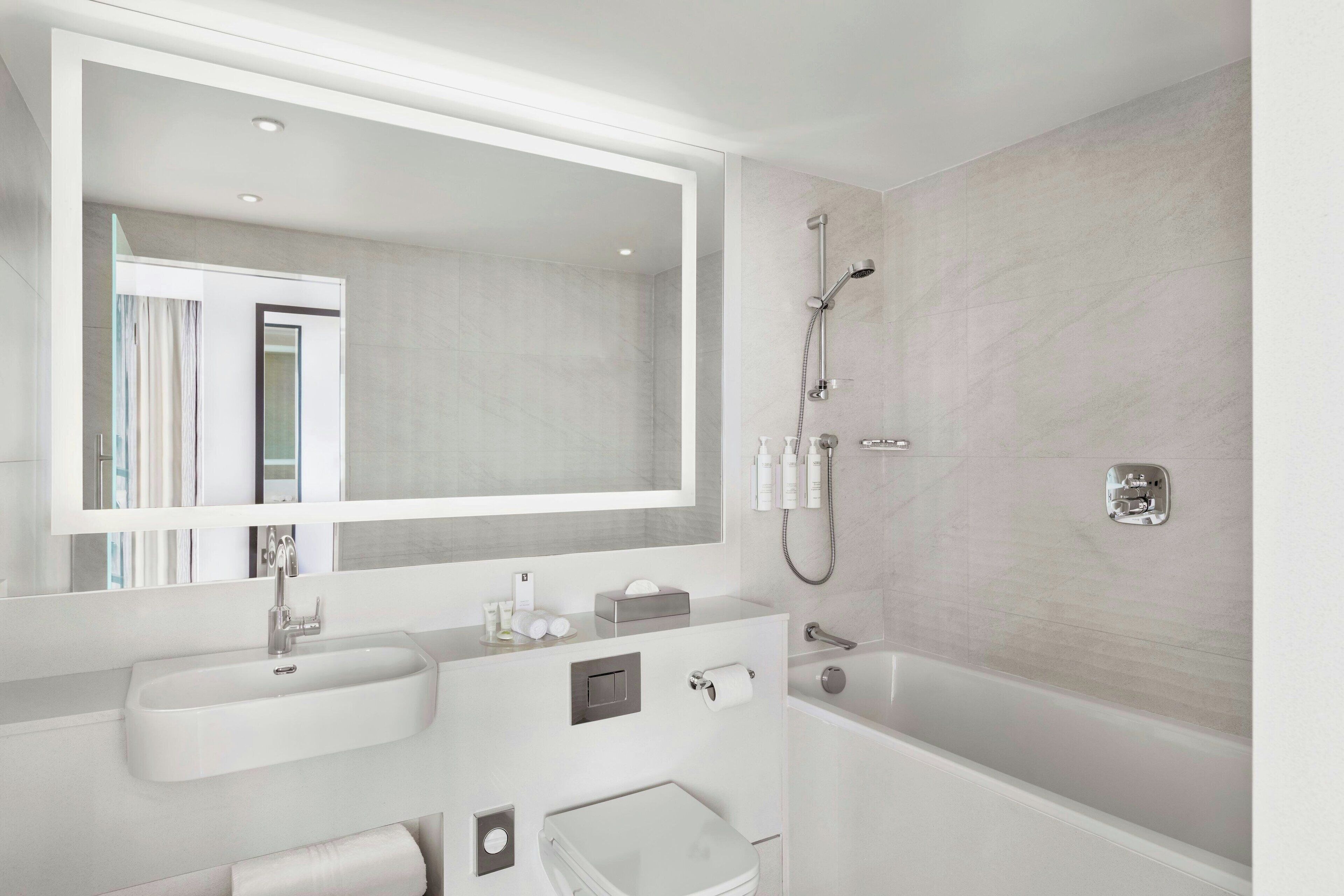 A modern bathroom with a large mirror, a sink, a toilet, and a bathtub.