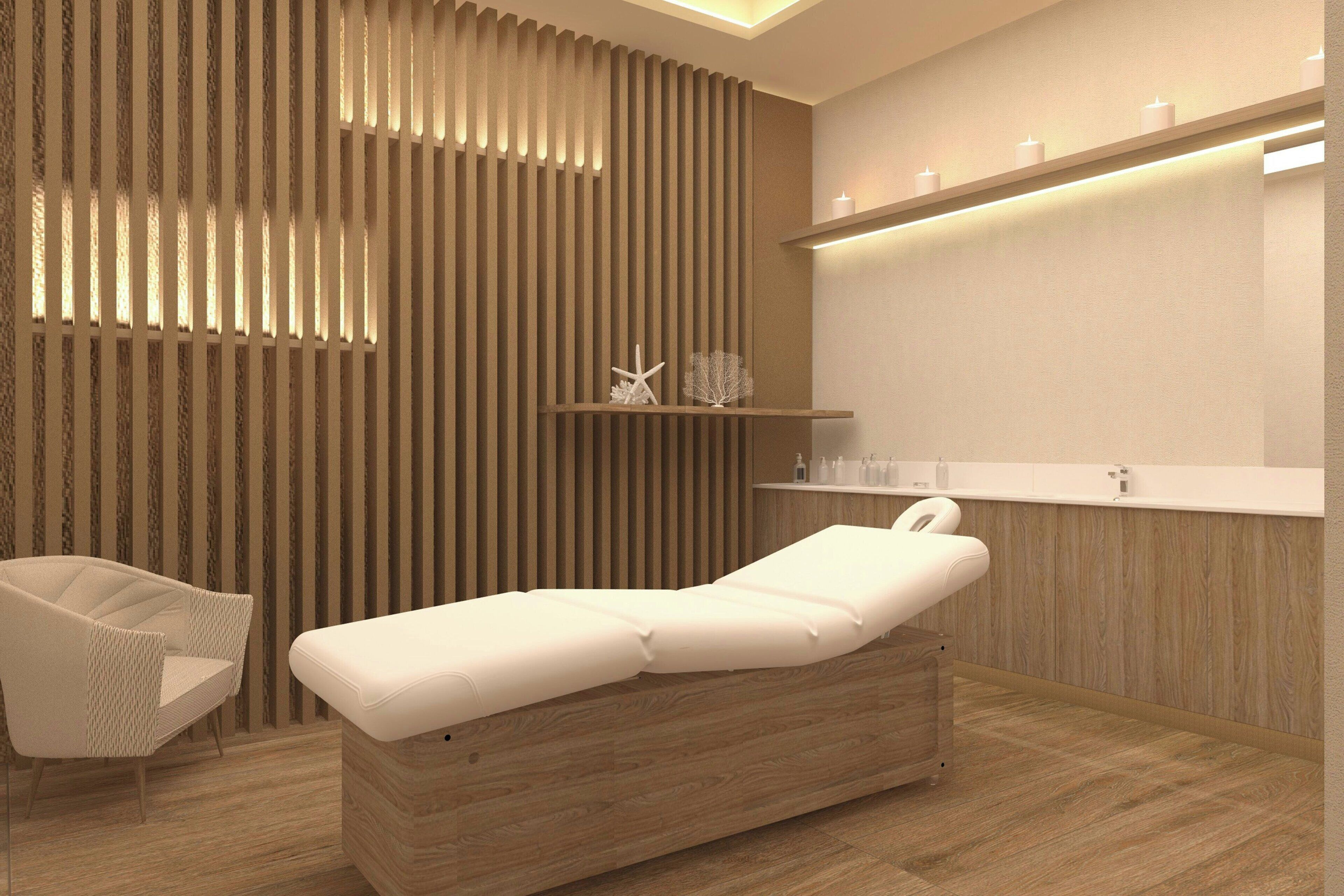 A modern medical examination room with a wooden panel wall, a white examination table, a white chair, and a shelf with candles and bottles.