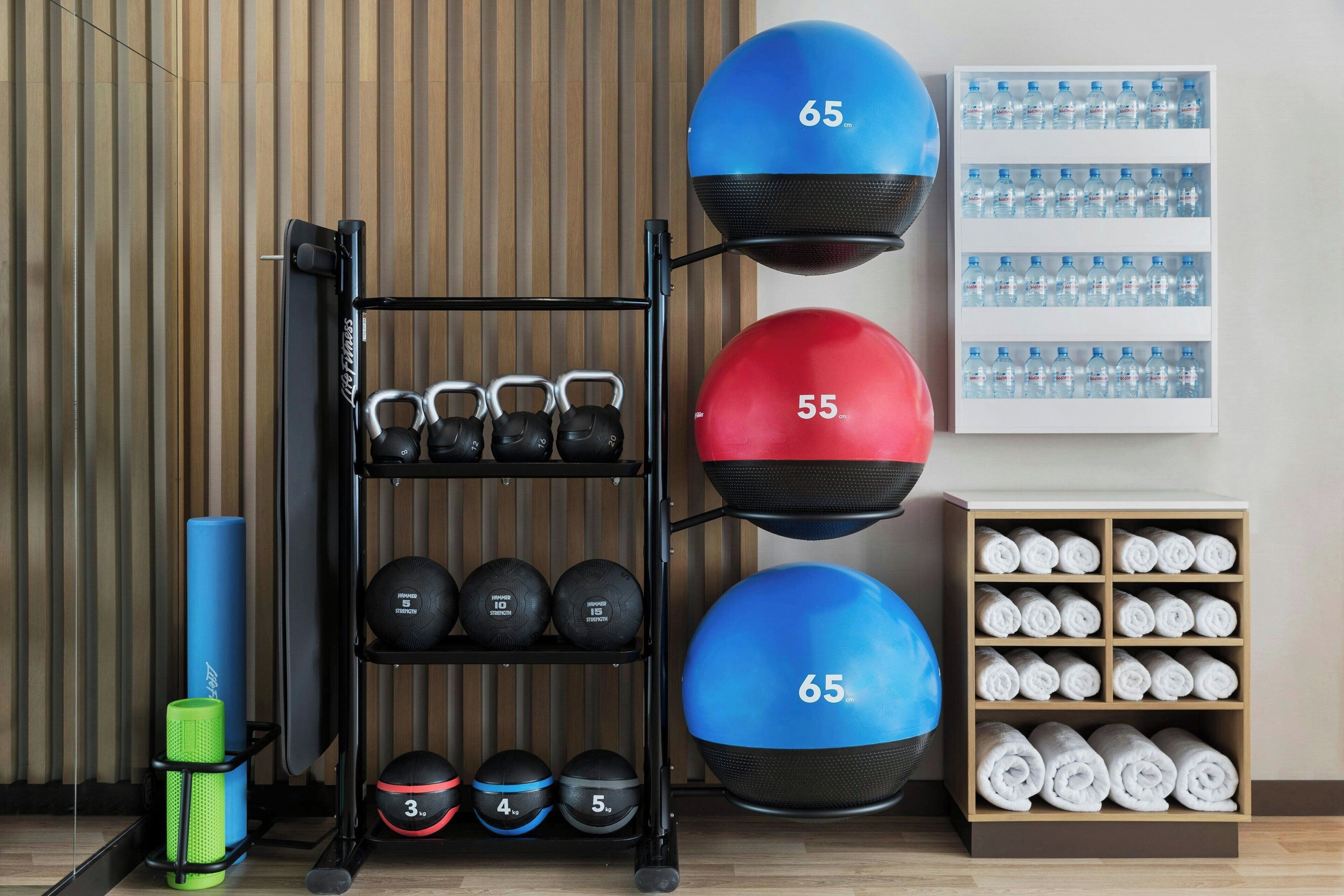 Un gimnasio con equipo de ejercicio, incluyendo pesas de cañón, balones medicinales y un dispensador de agua.