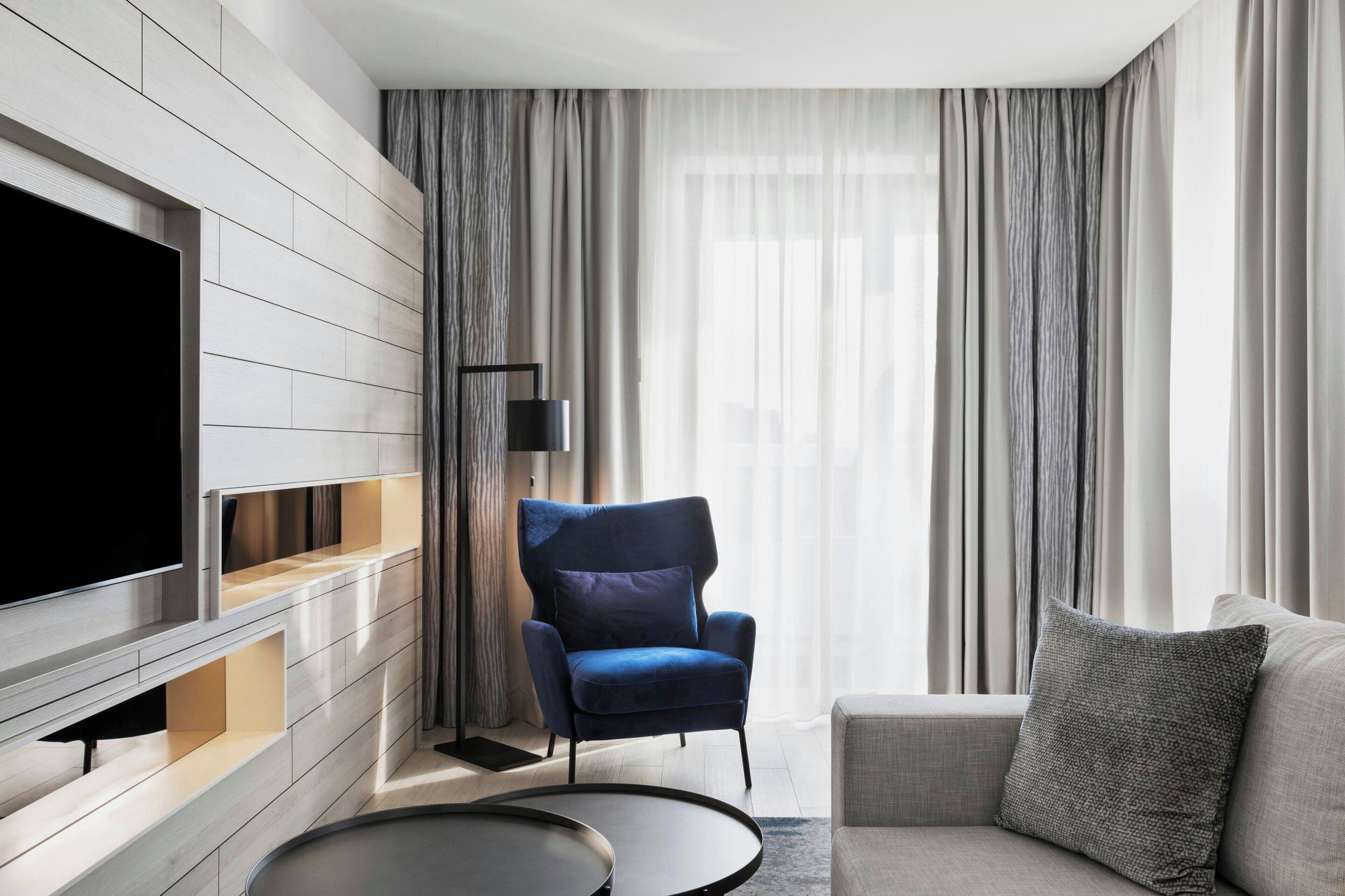 A modern living room with a flat-screen TV, a blue armchair, a grey sofa, and a round coffee table.