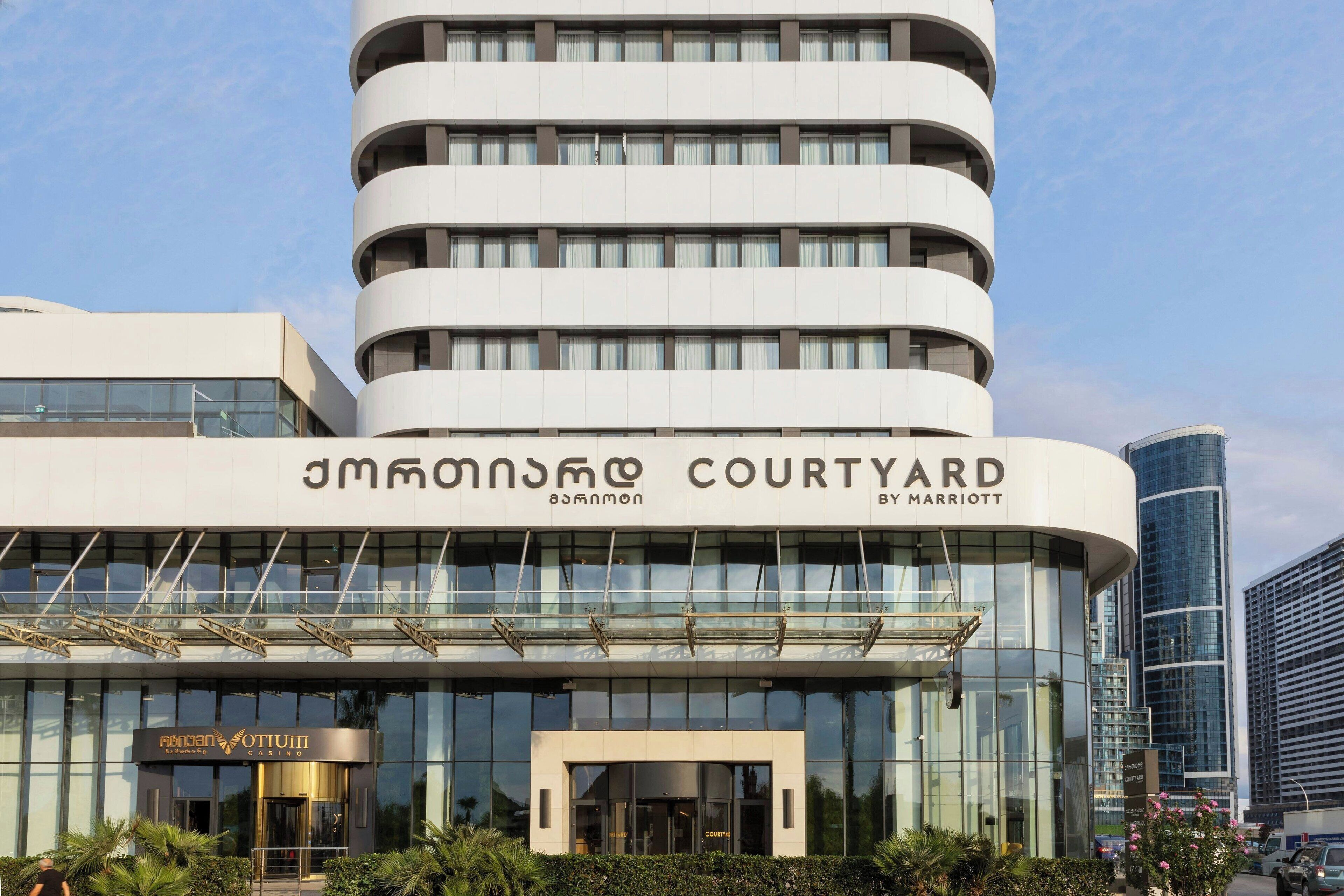 A modern hotel with a curved facade, multiple balconies, and a glass entrance.