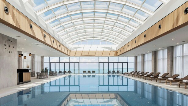 Una amplia piscina interior con tragaluces, sillas de descanso y vistas al mar.