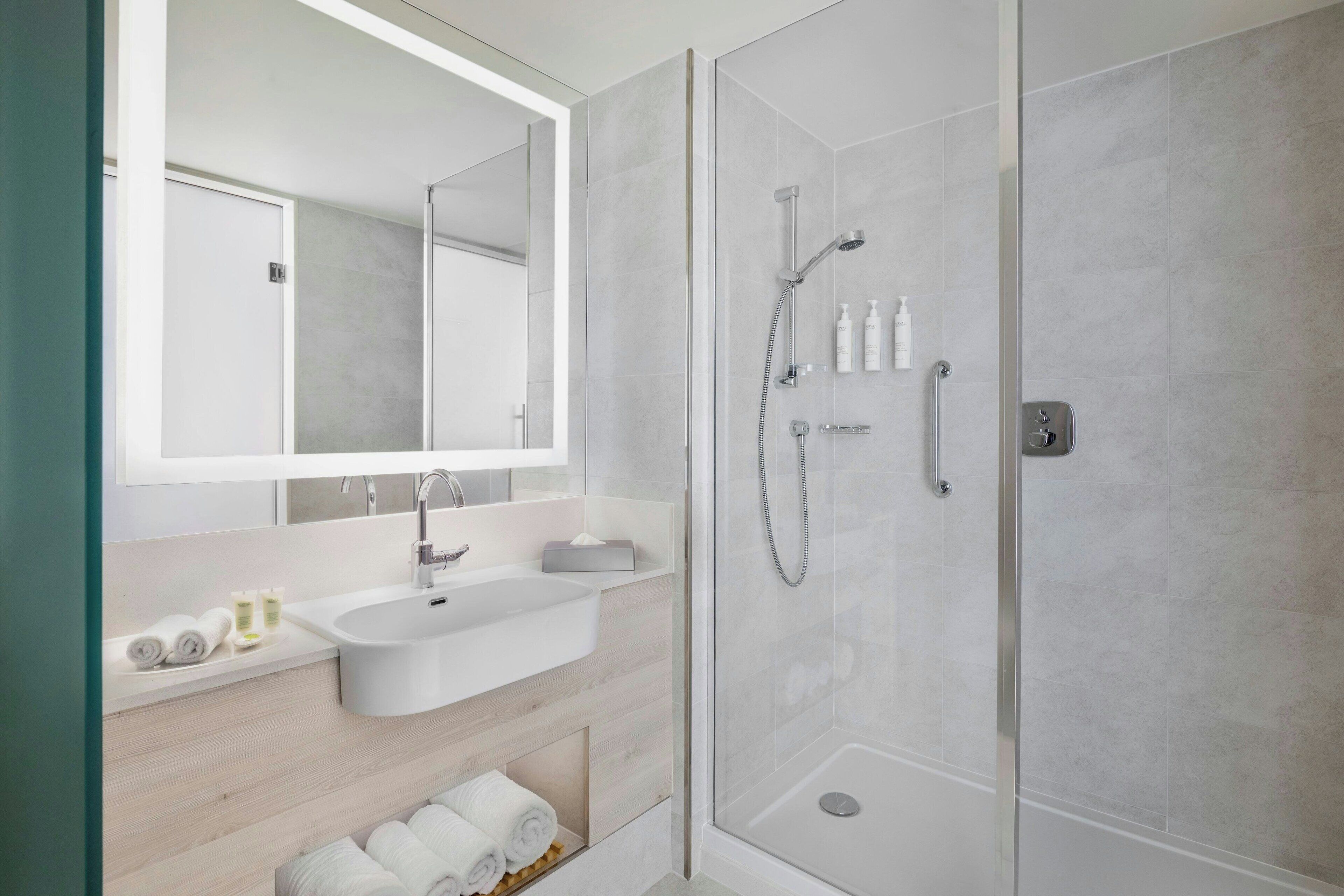 A modern bathroom with a large mirror, a sink, and a shower enclosure.