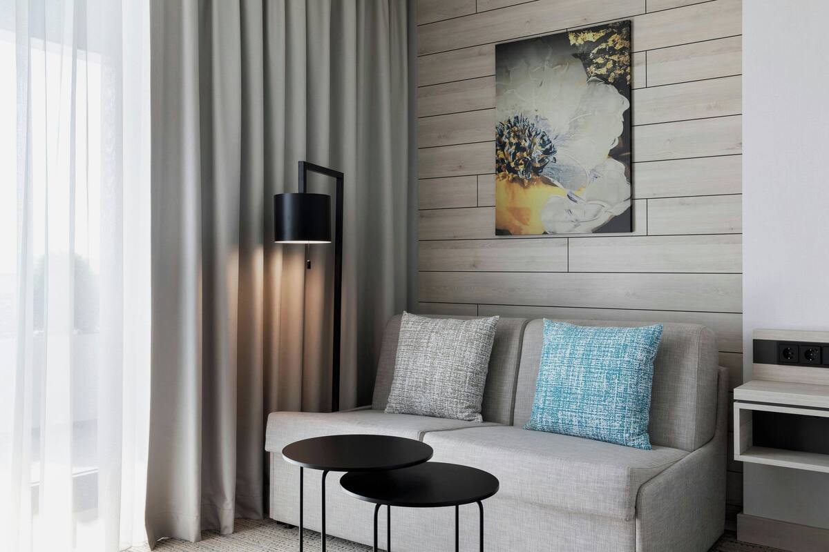 A modern living room with a grey sofa, two black side tables, a black floor lamp, and a painting on the wall.