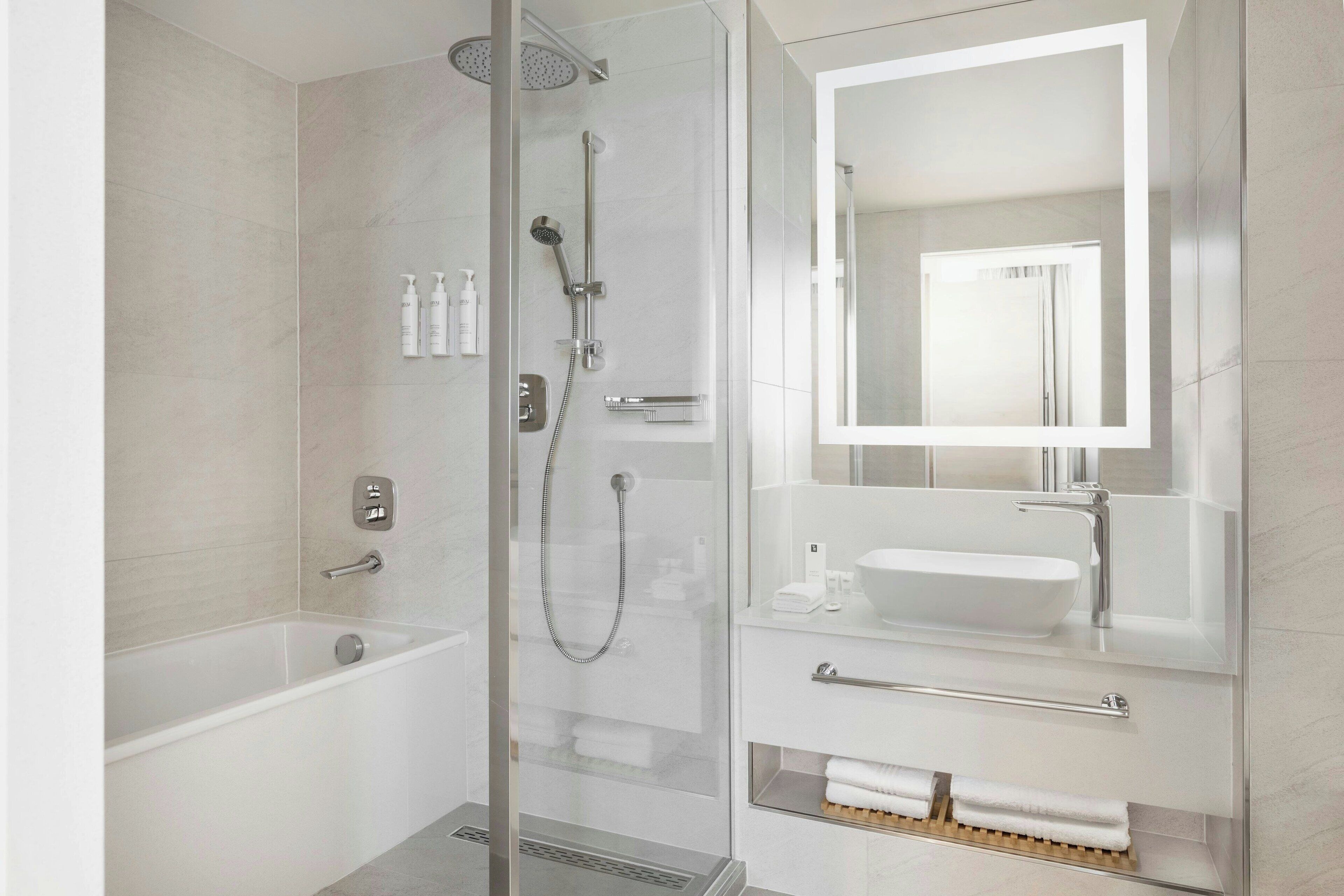 Un baño moderno con ducha de vidrio, bañera, tocador con lavabo y espejo.