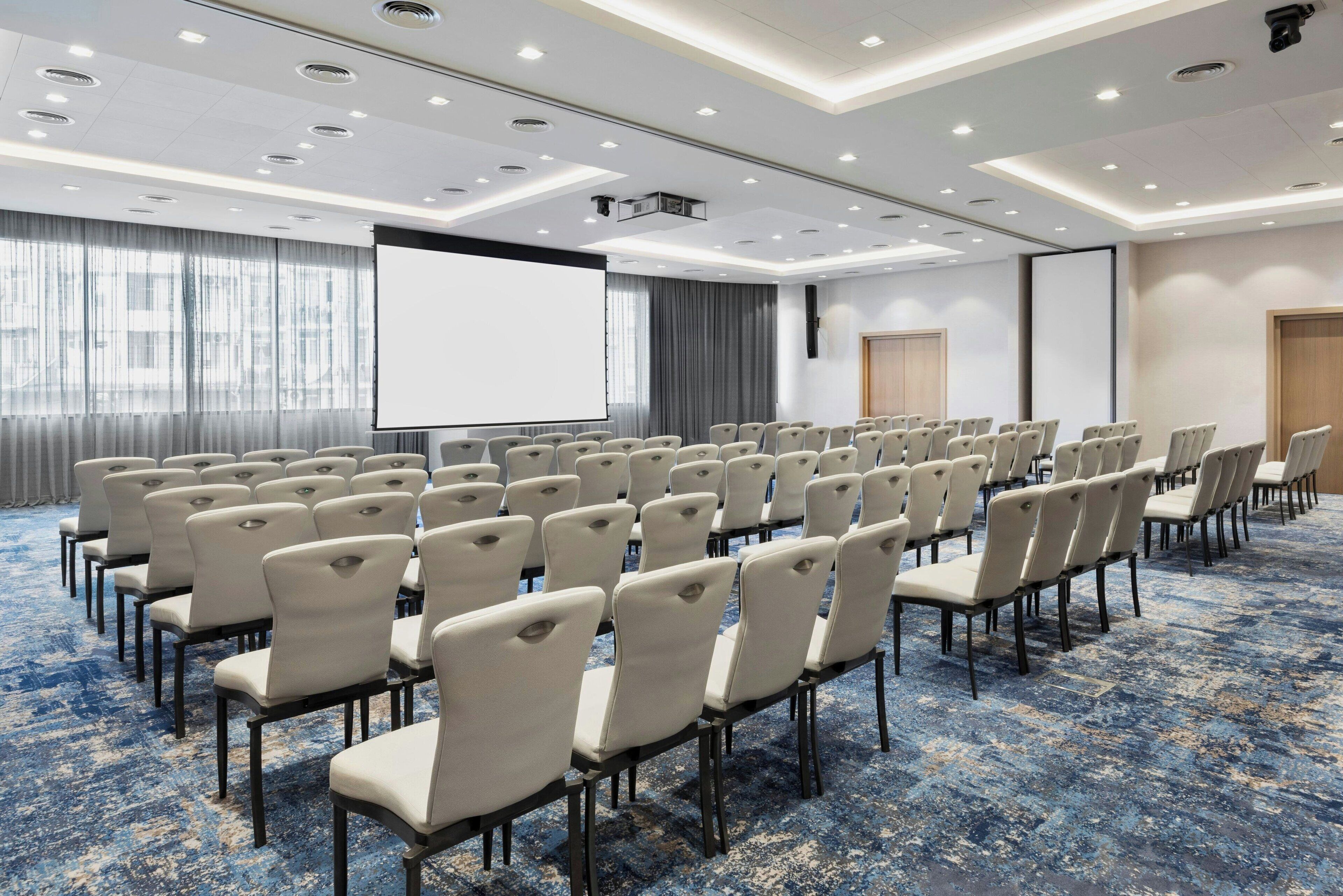 A conference room with rows of chairs, a large screen, and a projector.