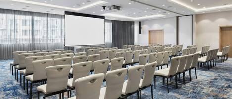A conference room with rows of chairs, a large screen, and a projector.