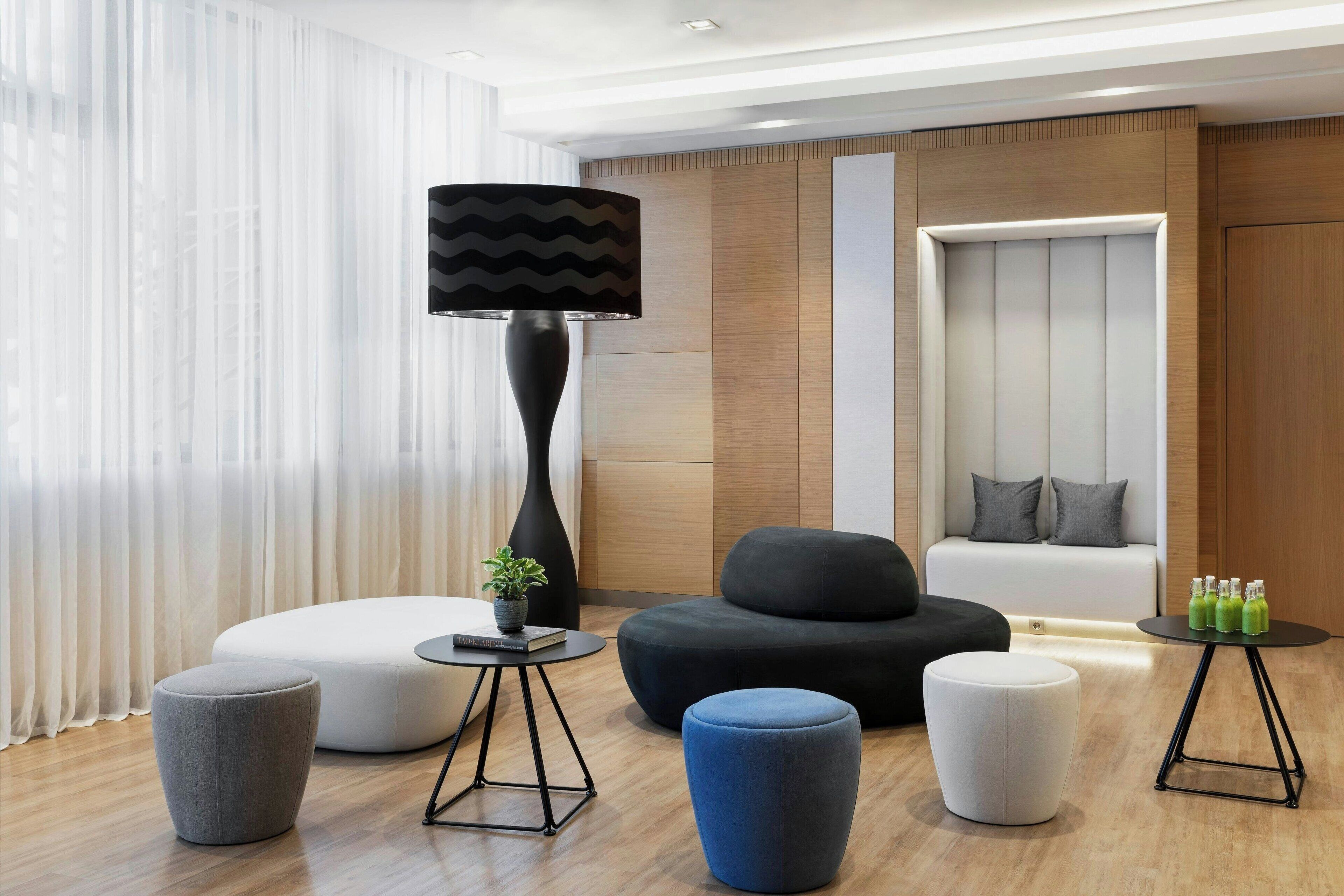 Un salon moderne avec un canapé, des poufs, une lampe et une petite table sur laquelle sont posées des bouteilles.