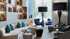 Un espacio lounge moderno con sofá, sillones y otomanas, chimenea y un ventanal con vistas a la ciudad.