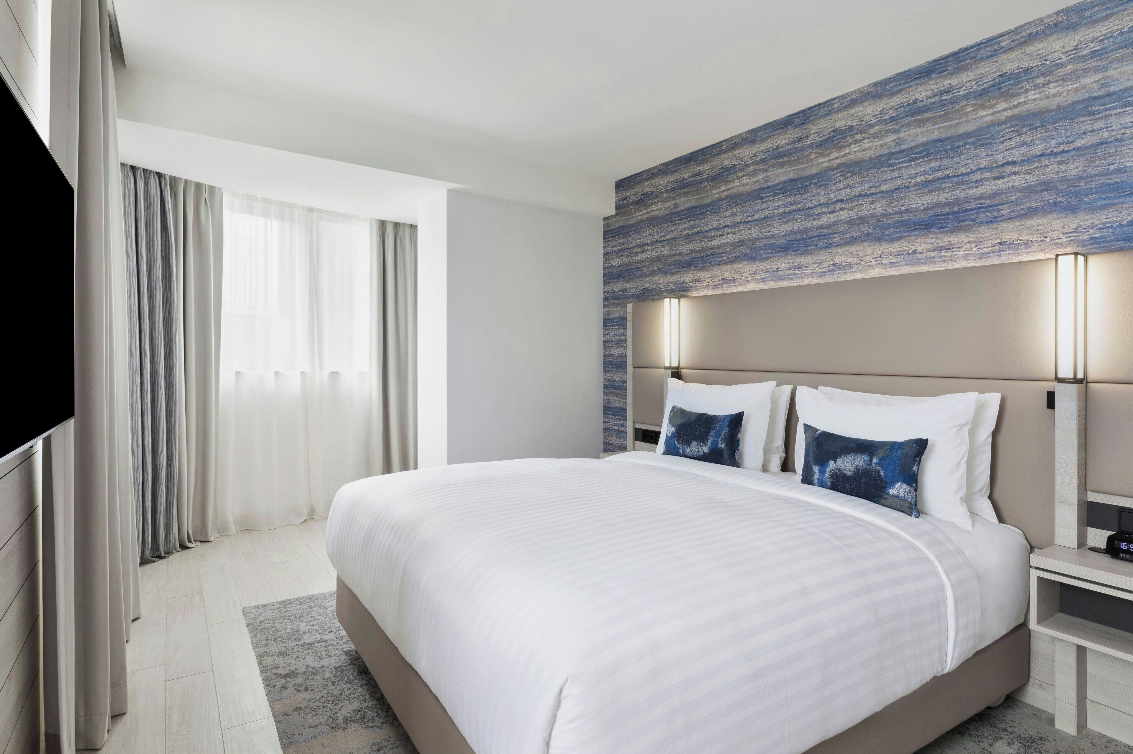 A modern hotel room with a large bed, a flat-screen TV, and a view of the outdoors.