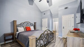 Een slaapkamer met een bed, nachtkastje, dressoir, plafondventilator en een deur.