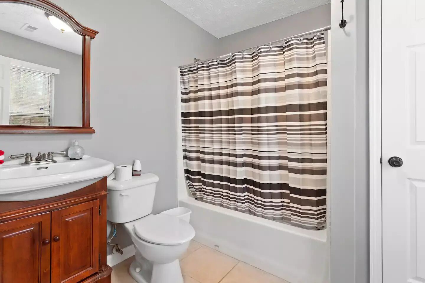 A bathroom with a wooden vanity, a white sink, a toilet, and a striped shower curtain.