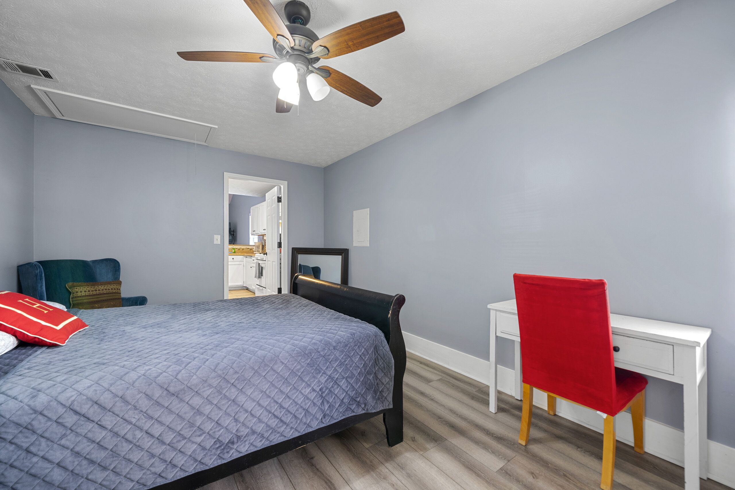 A bedroom with a bed, a desk, a chair, and a ceiling fan.