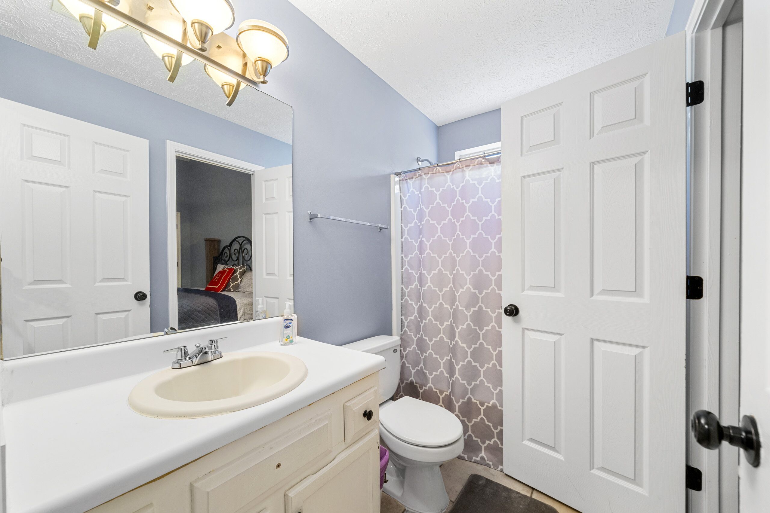 A bathroom with a white sink, a mirror, a toilet, and a shower curtain.