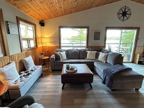Una sala de estar acogedora con un sofá modular, una mesa de centro y una lámpara. Hay ventanas que dejan entrar luz natural y ofrecen vistas al exterior.
