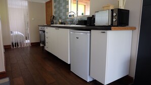 Cocina compacta con armarios blancos, lavavajillas, microondas y cafetera en la encimera.