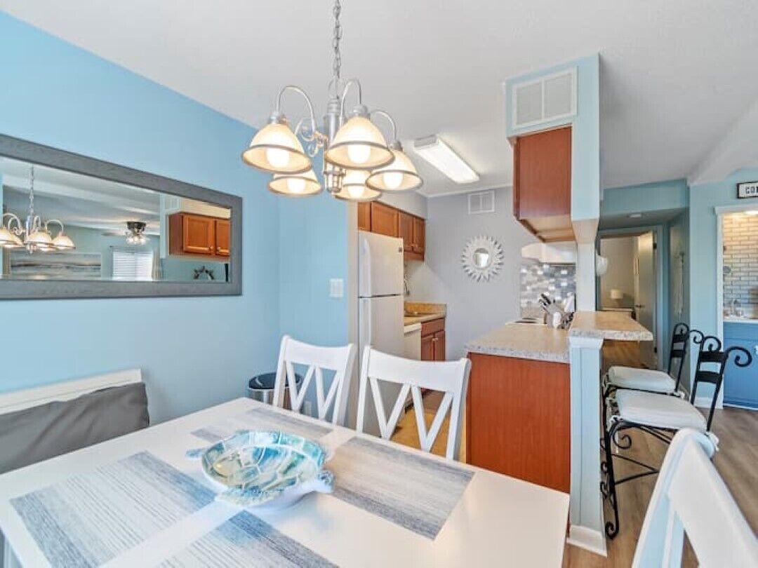 Une cuisine moderne avec des meubles blancs, un îlot central et un coin repas comprenant une table et des chaises.