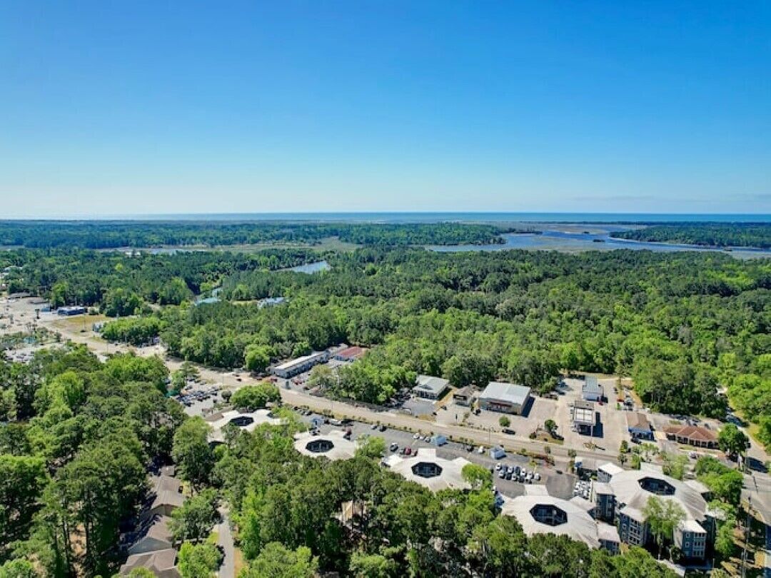 An aerial view of a coastal town with dense greenery, a marina, and a mix of commercial and residential buildings.