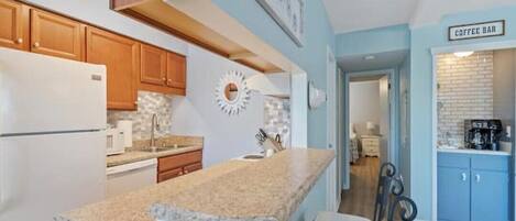 A kitchen with wooden cabinets, a granite countertop, and a coffee bar area.
