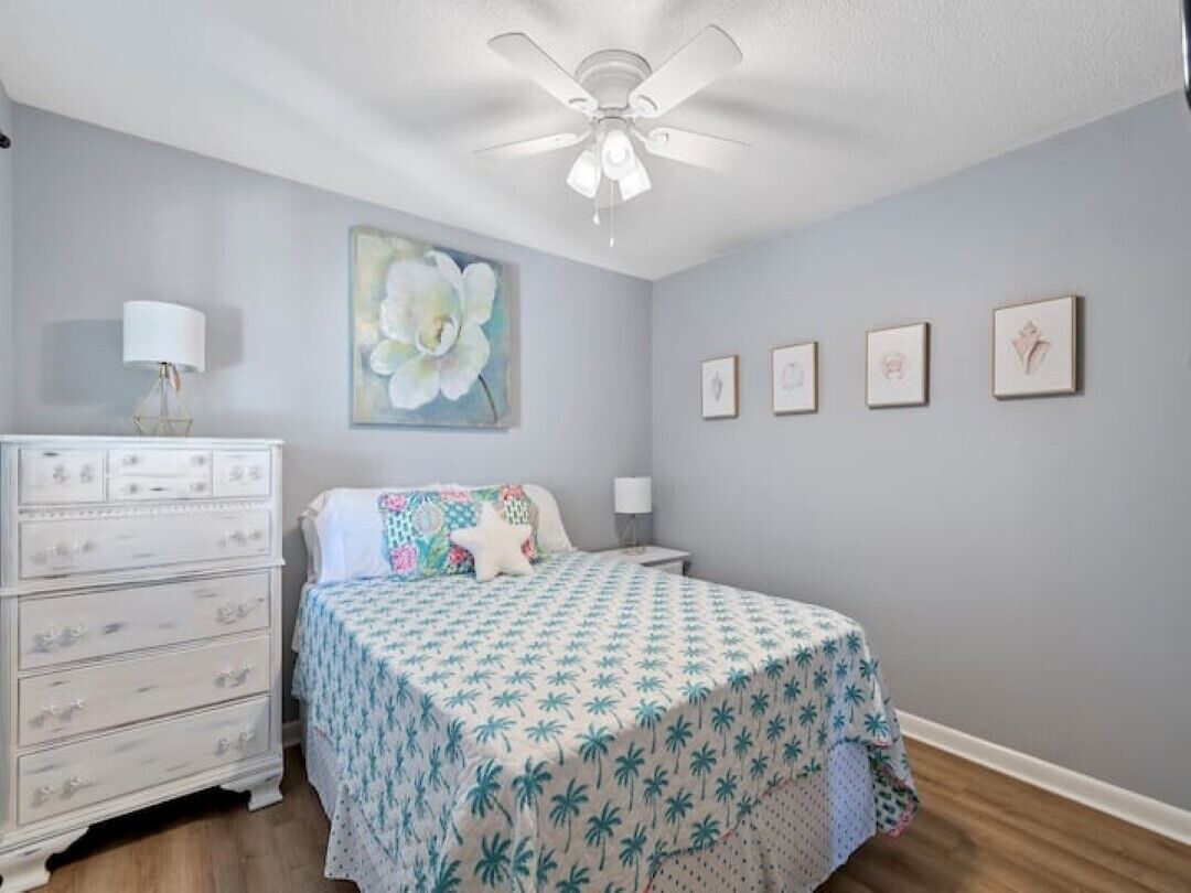 Een slaapkamer met een bed, een dressoir, een plafondventilator, wanddecoratie en ingelijste foto's.