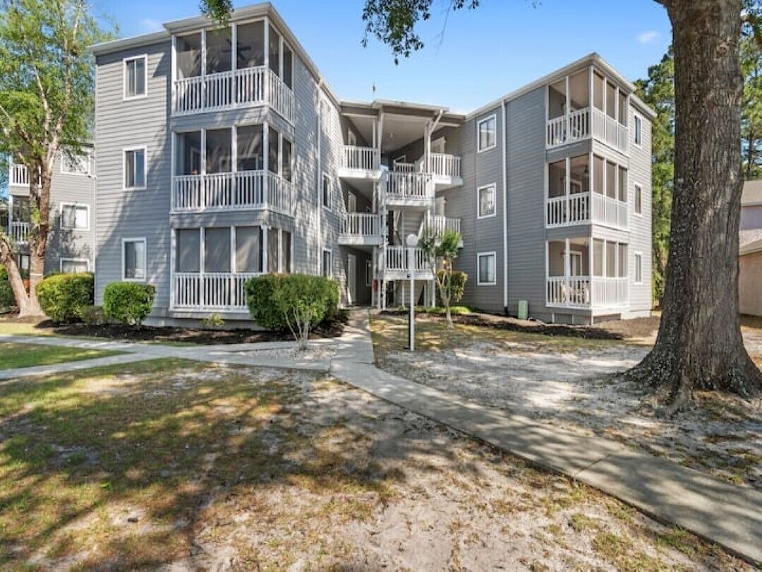 A multi-story residential building with balconies, a central courtyard, and a tree-lined driveway.
