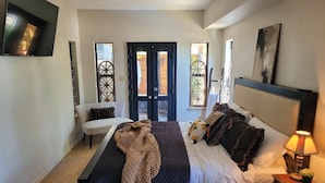 A bedroom with a bed, bedside table, lamp, and a view of the outside through a door.