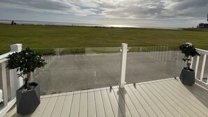 Une terrasse en bois avec une rambarde, des plantes en pot et une vue sur l’océan.