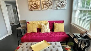 Een kamer met een rode bank, een grijze poef en drie bloemschilderijen die aan de muur hangen.