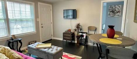 A living room with a sofa, ottoman, dining table, chairs, a TV, and a door.