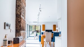 Una cocina moderna con un detalle de pared de piedra, una zona de comedor con sillas azules y vistas al exterior.