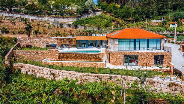 Una villa moderna con fachada de piedra, piscina y vistas a las colinas circundantes.