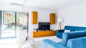 Un salón moderno con una televisión grande, armarios de madera, un sofá azul y un sillón blanco.